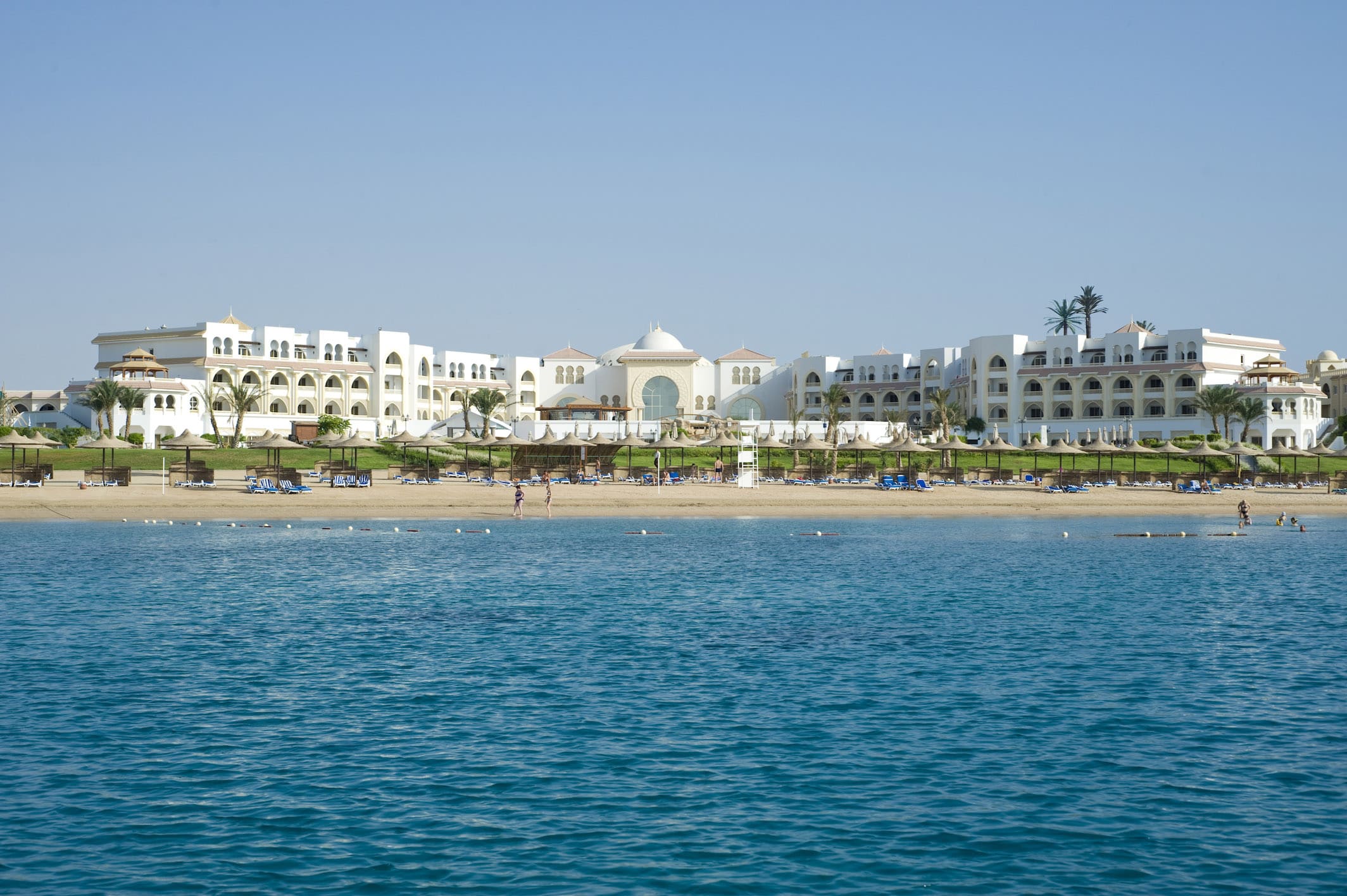 Old Palace Resort overlooks the beach, with a large white building and blue sea in the foreground.