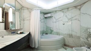 Marble-walled bathroom, corner tub, curtain, and vanity mirror at Hurghada Marriott Beach Resort.