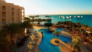 Hurghada Marriott pool area with palm trees overlooks a calm sea and boats at sunset.