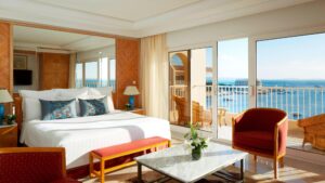 Hotel room with a bed, chairs, and a balcony overlooking the sea at Hurghada Marriott Beach Resort.