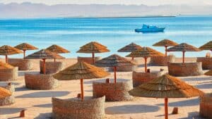 Beach at Sheraton Soma Bay with straw umbrellas, wicker seating, and a boat on the water.