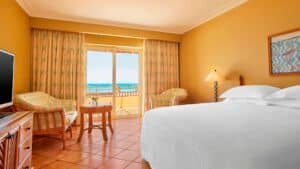 Sheraton Soma Bay room with bed, chairs, table, TV, and ocean-view balcony.