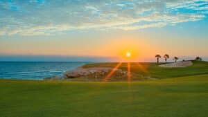 Sunset over Sheraton Soma Bay golf course with palm trees and a sand trap by the sea.