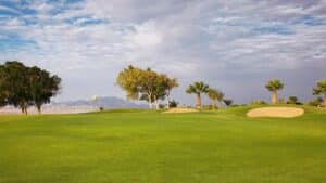 Sheraton Soma Bay golf course with sand trap, trees, and distant mountains under a cloudy sky.