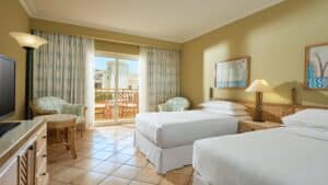 Sheraton Soma Bay hotel room with two beds, TV, chairs, and patio access.