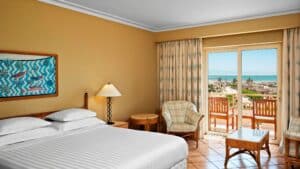 Sheraton Soma Bay hotel room with a large bed, chairs, a table, and sea-view balcony.