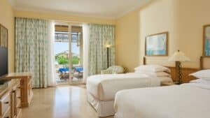 Sheraton Soma Bay room with two beds, TV, and balcony featuring outdoor chairs and a view.