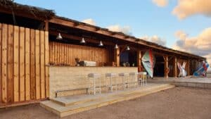 Sheraton Soma Bays outdoor bar features wooden stools and surfboards by a sandy beach.