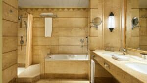 A Sheraton Soma Bay bathroom with a bathtub, shower, double sink, and beige tile walls.