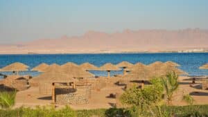 Sheraton Soma Bays beach with thatched umbrellas, calm sea, and distant mountains.