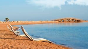 Empty beach with lounge chairs at Sheraton Soma Bay, facing the calm sea and distant wooden bridge.