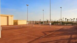 Empty outdoor tennis court at Sheraton Soma Bay, with brown surface and palm trees.