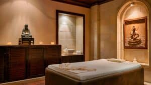 A serene Sheraton Soma Bay spa room with a massage table, statues, candles, and wooden cabinet.