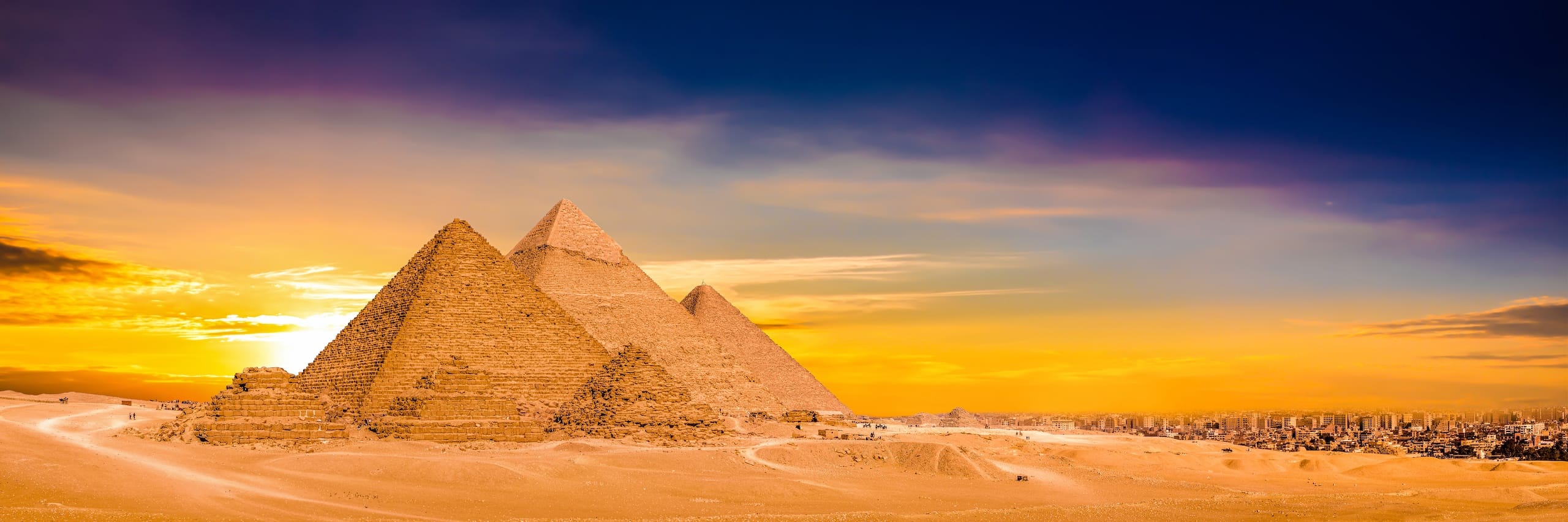Classic Egypt unfolds as the Pyramids of Giza glow at sunset, city skyline beyond.