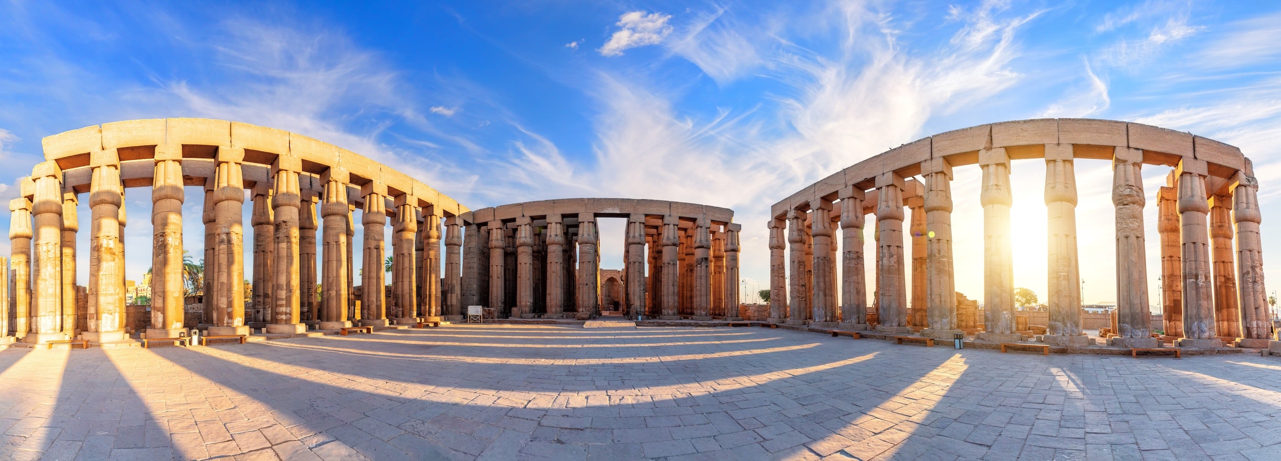 Panoramic view of ancient stone columns under a blue sky with scattered clouds.