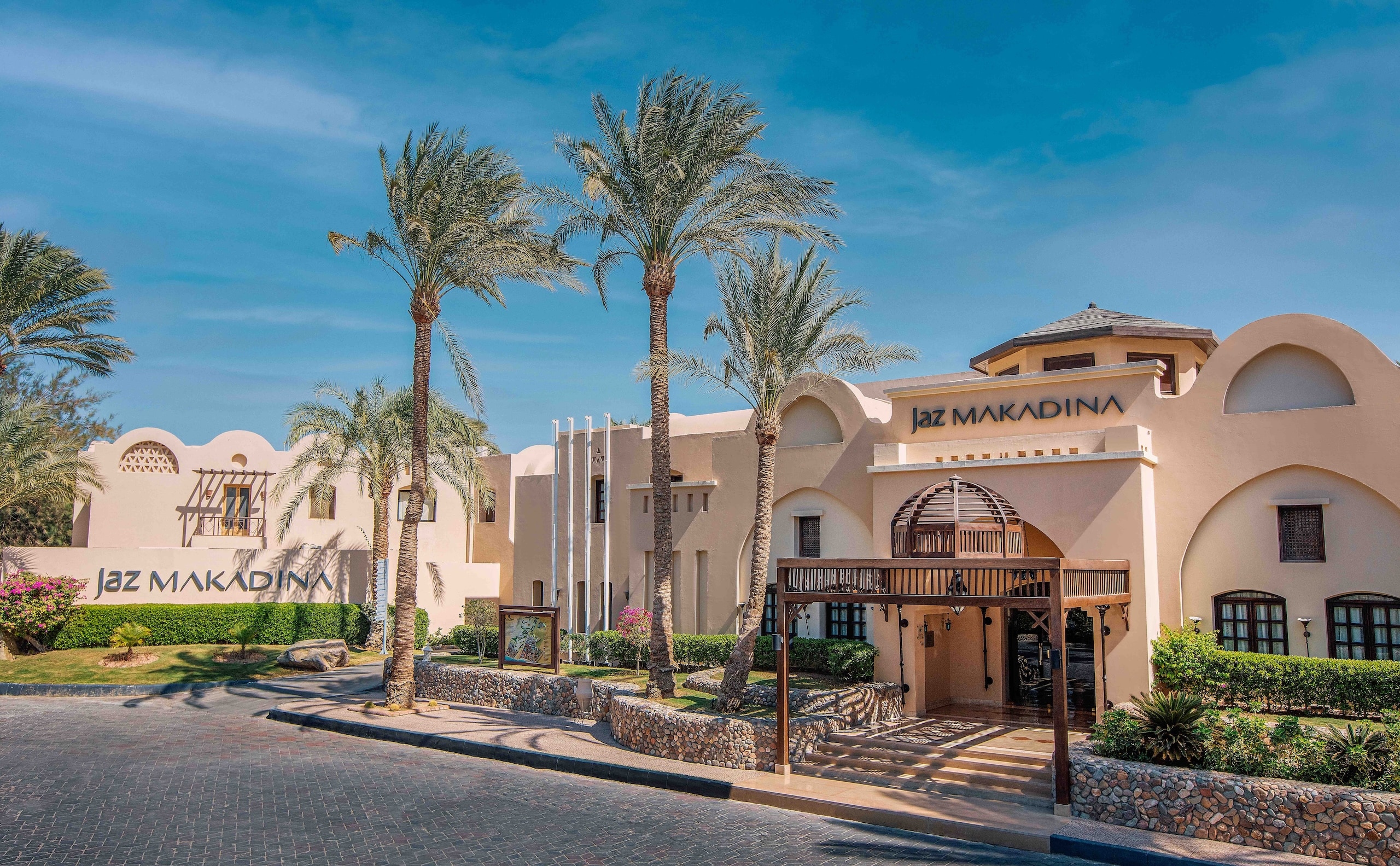Jaz Makadinas exterior graced by palm trees under a clear sky.