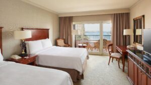 Room at Cairo Marriott Hotel with two beds, TV, desk, chairs, and a balcony overlooking water.