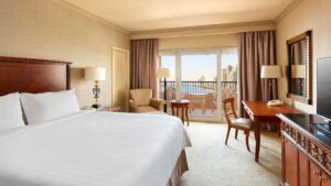 Room with a bed, desk, chair, and balcony overlooking Cairo Marriotts city view.
