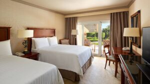 Hotel room at Cairo Marriott with two beds, a desk, and garden patio views through glass doors.