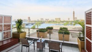 Cityscape view from a balcony at The Nile Ritz-Carlton, overlooking a river with chairs and table.