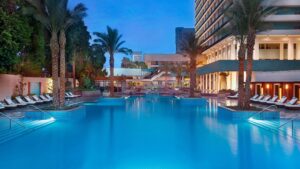 The Nile Ritz-Carlton hotel pool, framed by palm trees, shines at dusk beside the towering building.