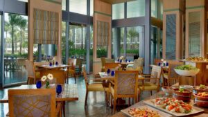 A spacious interior at The Nile Ritz-Carlton with wooden tables, chairs, and a buffet setup.