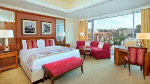 The Nile Ritz-Carlton room with a large bed, sofa, desk, and city view.