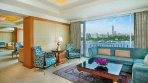 Elegant hotel room at The Nile Ritz-Carlton, featuring blue chairs and a city view through a large window.