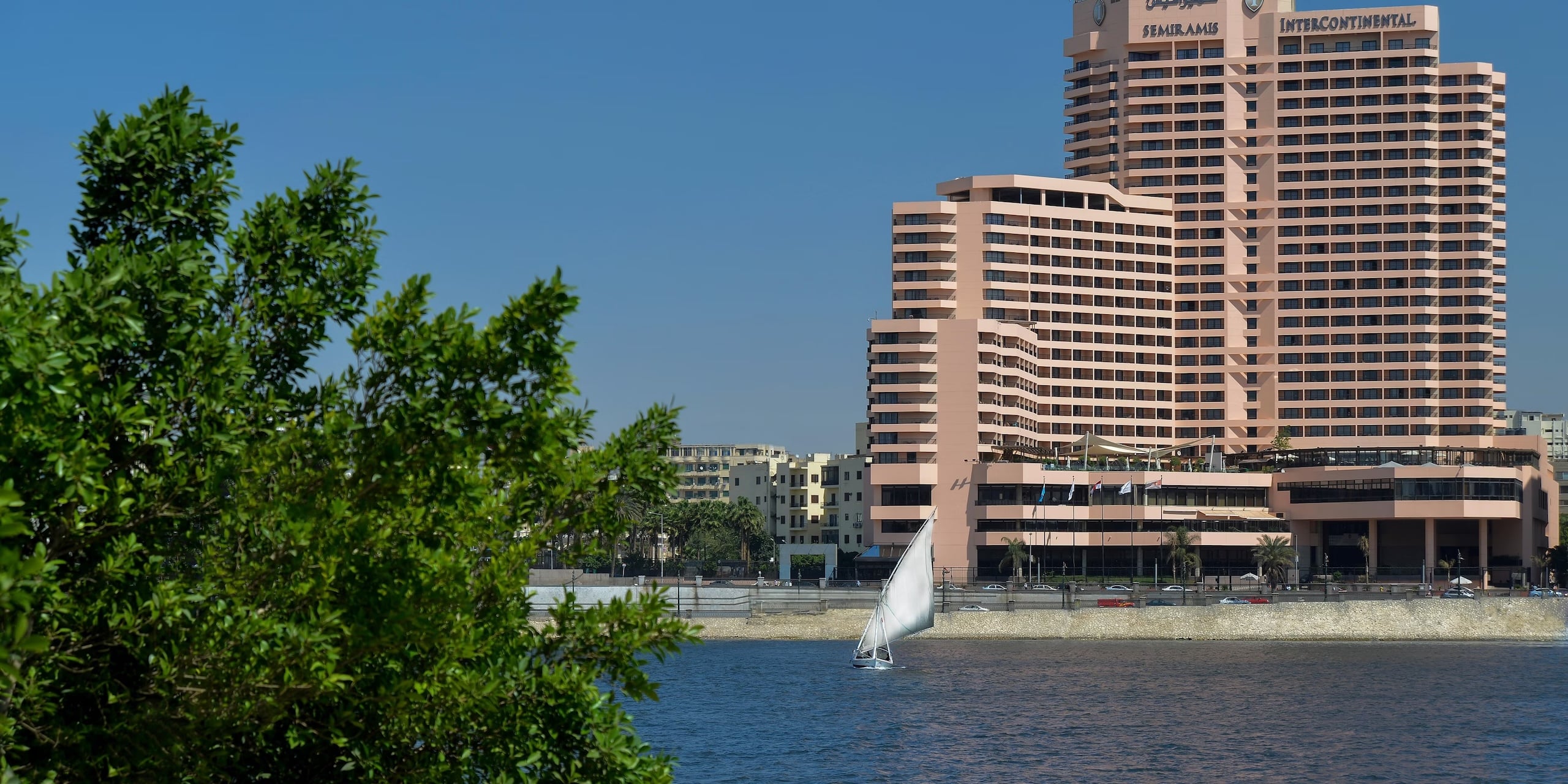 Sailboat on river by InterContinental Semiramis, with greenery in the foreground.