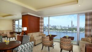 The Nile Ritz-Carlton lounge with river view, cityscape, and a distant tall tower.