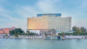 The Nile Ritz-Carlton by the water with palm trees and a clear sky.