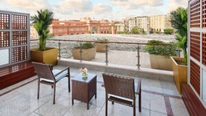 Terrace at The Nile Ritz-Carlton with wicker chairs, table, and potted plants overlooking a cityscape.