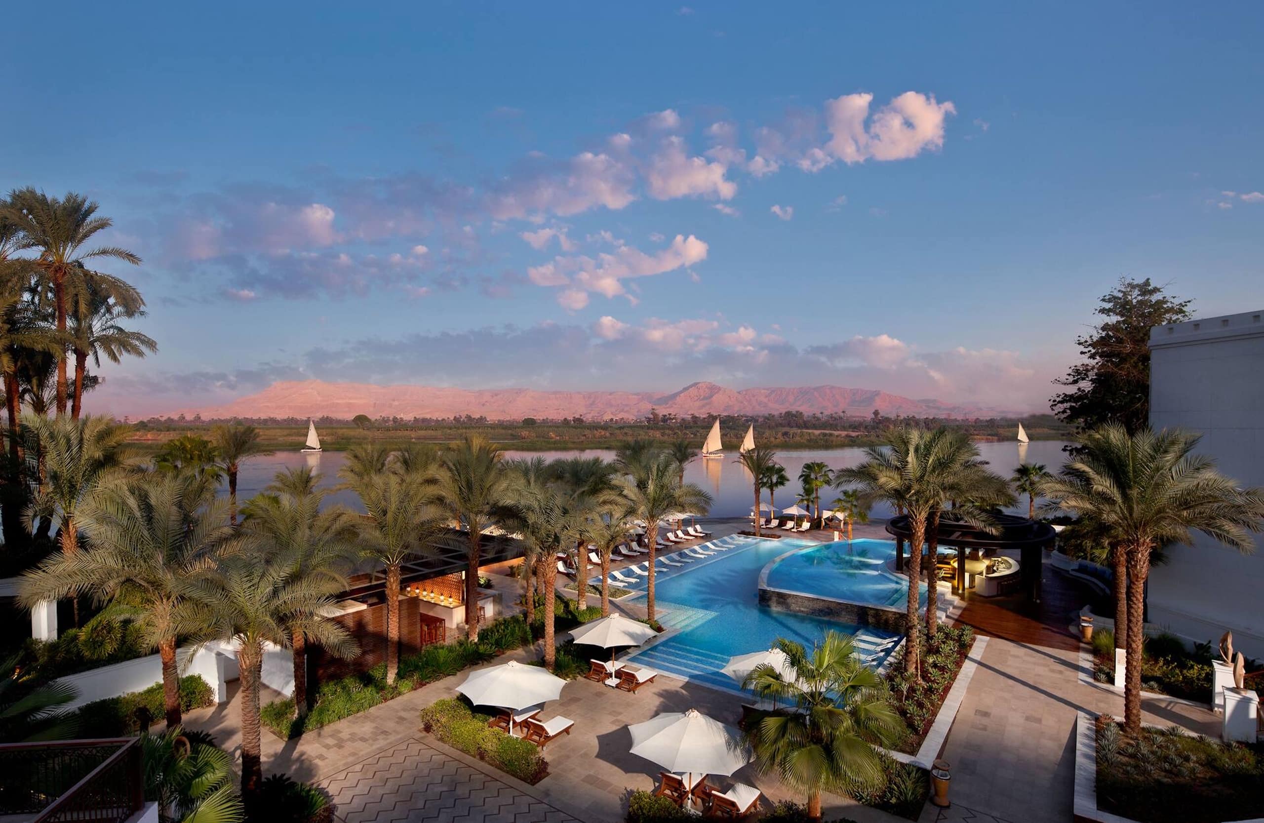 Hilton Luxors pool, palm-fringed with lounge chairs, overlooks sailboats on the serene river.